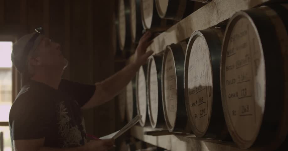 A distillery worker examines barrels of whiskey