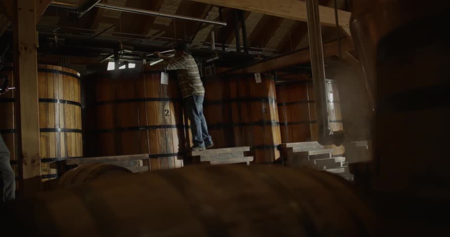A man is checking a barrel of beer in a distillery