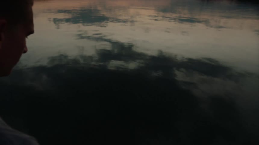 Person stands over calm waters staring down
