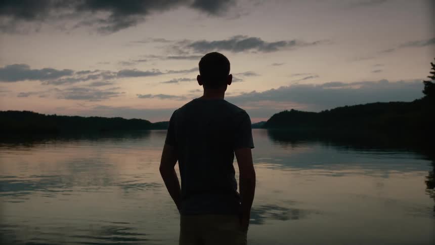 A silhouette of a man looking out over a lake