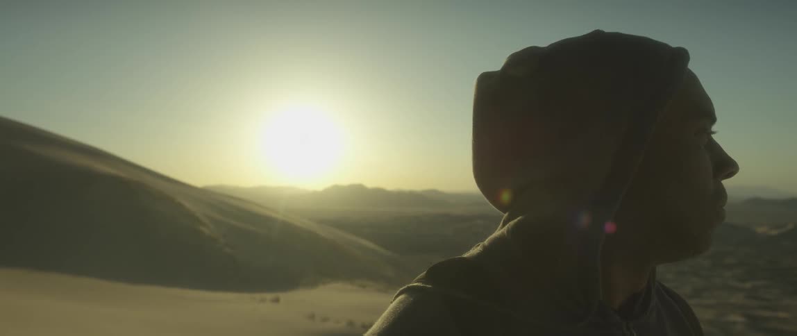 A man in a hoodie stands near a dune