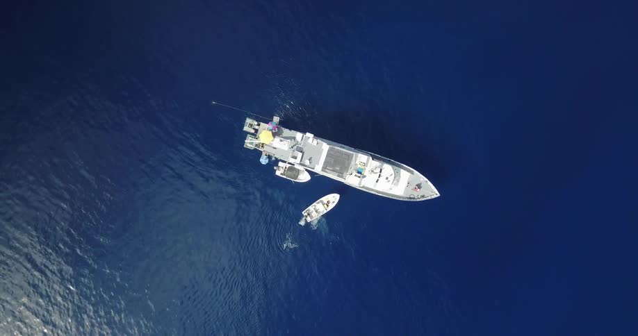 A small boat next to a larger boat in blue water
