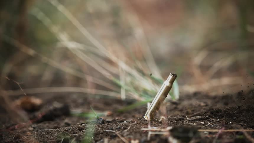 A bullet casing falls into the dirt
