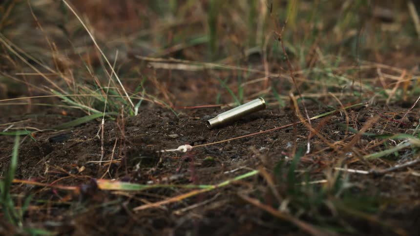 A spent bullet casing falls to the ground