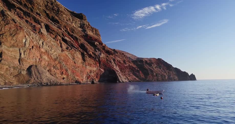 A small boat sits in a secluded bay near a beach surrounded by cliffs