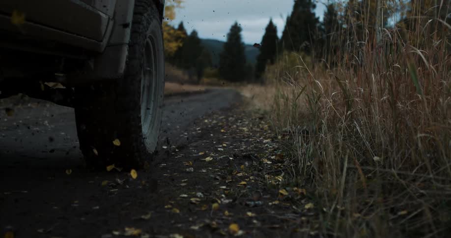 A vehicle drives on a rural road and kicks up leaves and dirt