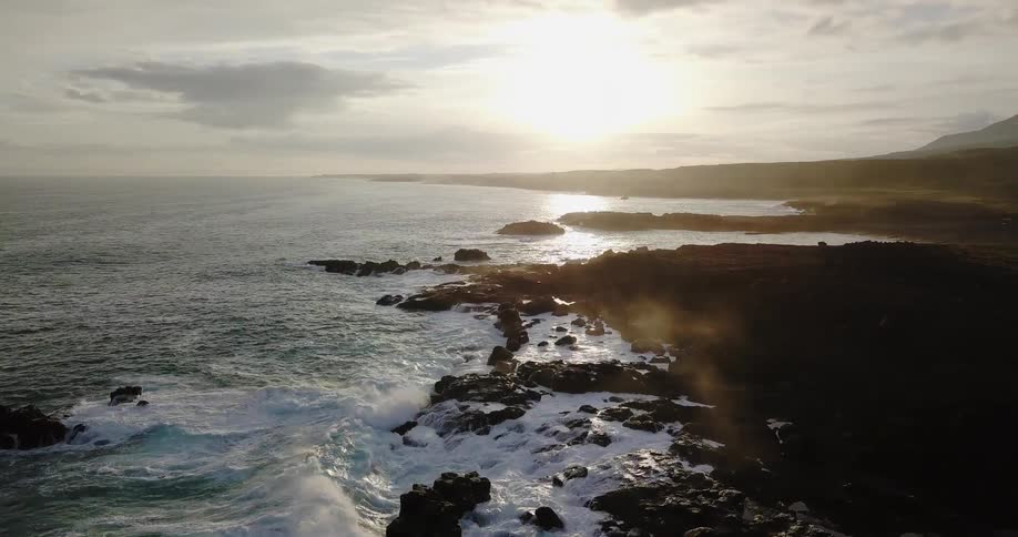 Waves crash and break against the rocky coast at sunset