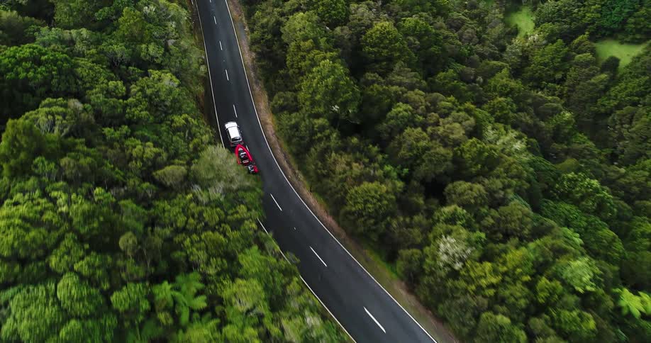 An suv towing a boat winds along a two-lane road in a forest