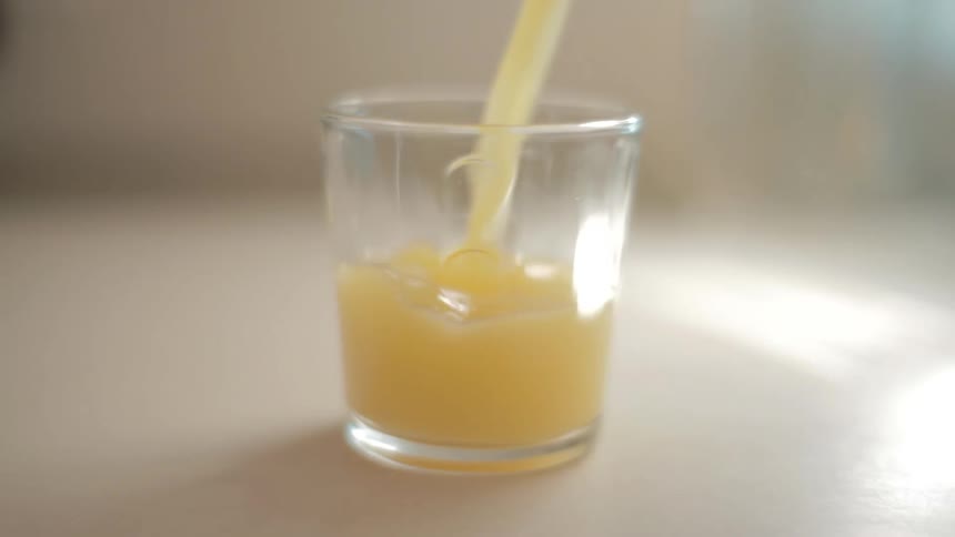 Orange juice being poured into a small glass