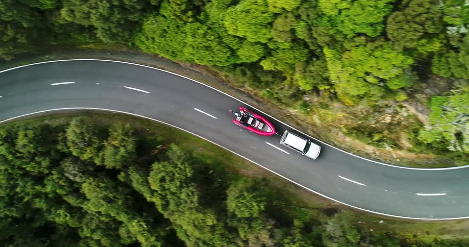 An suv towing a boat winds along a two-lane road in a forest