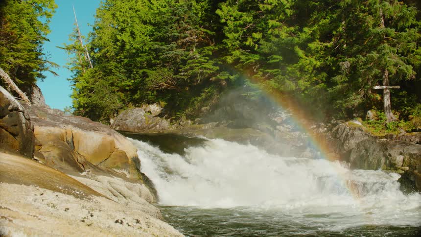 A river gushes beneath a rainbow on a sunny day
