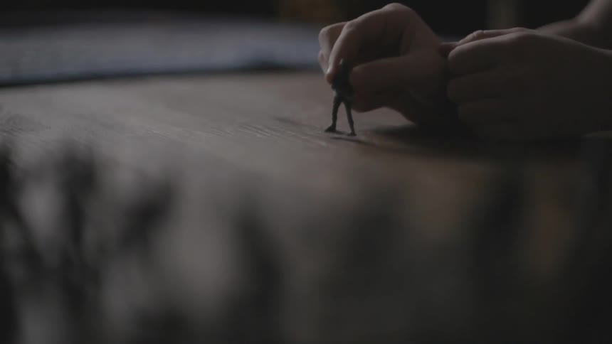 Hand tapping an army guy toy on a wooden surface
