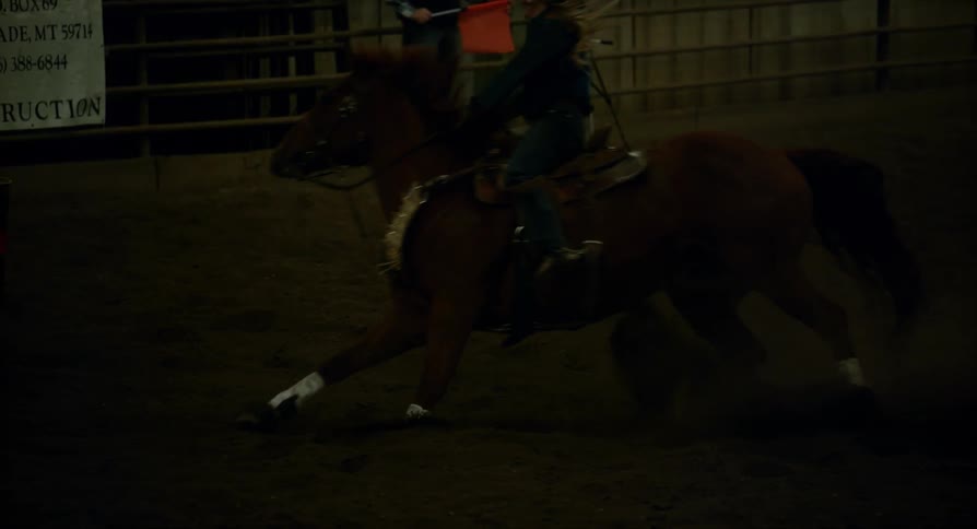 Man waves a red flag inside of a barn and a horse runs past