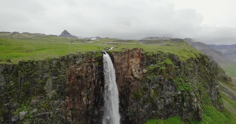 A waterfall flows over steep, jagged cliffs in a green valley