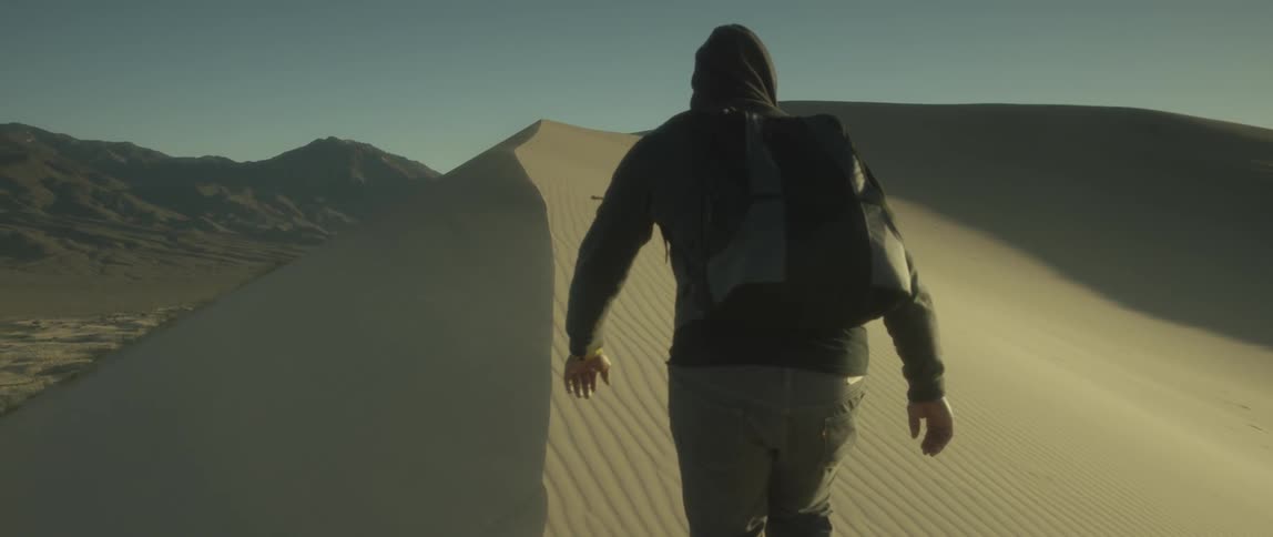 Man wearing backpack begins traveling up a steep sand dune