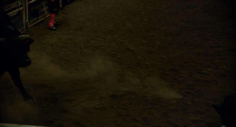 A cowboy rides a bucking bull at a rodeo