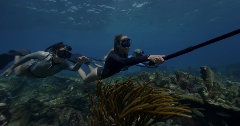 A female snorkeler holds a camera on a pole as she and her friends swim in the ocean