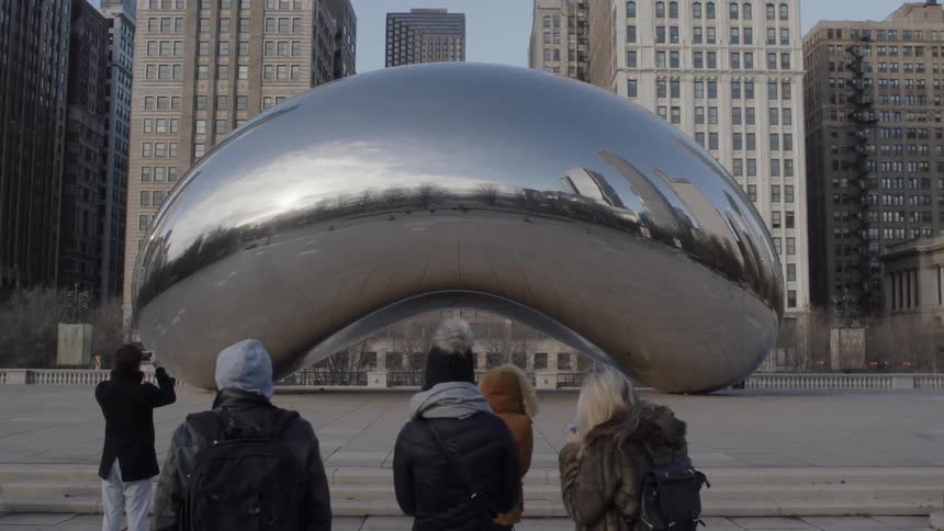 Tourists are taking pictures of a giant silver bean in a city on a cold day