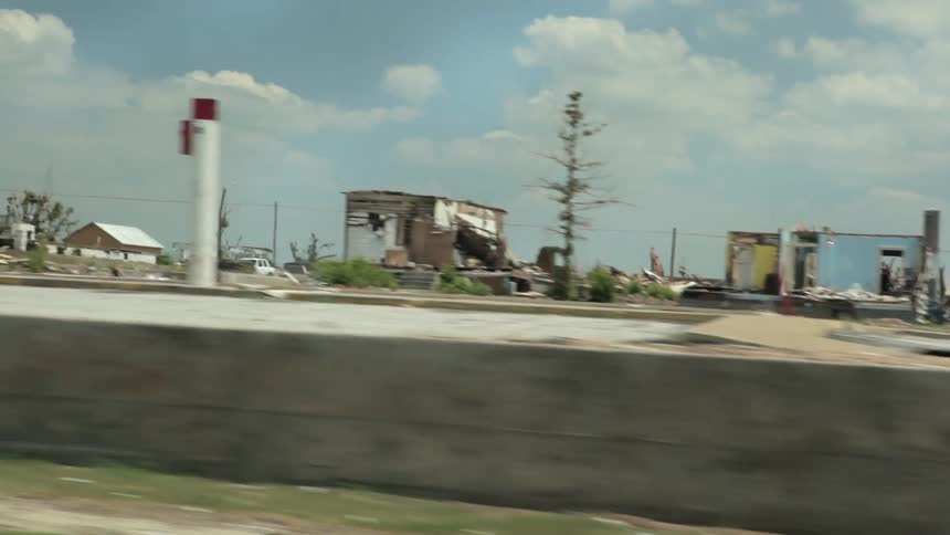 A car driving past damage done by a tornado