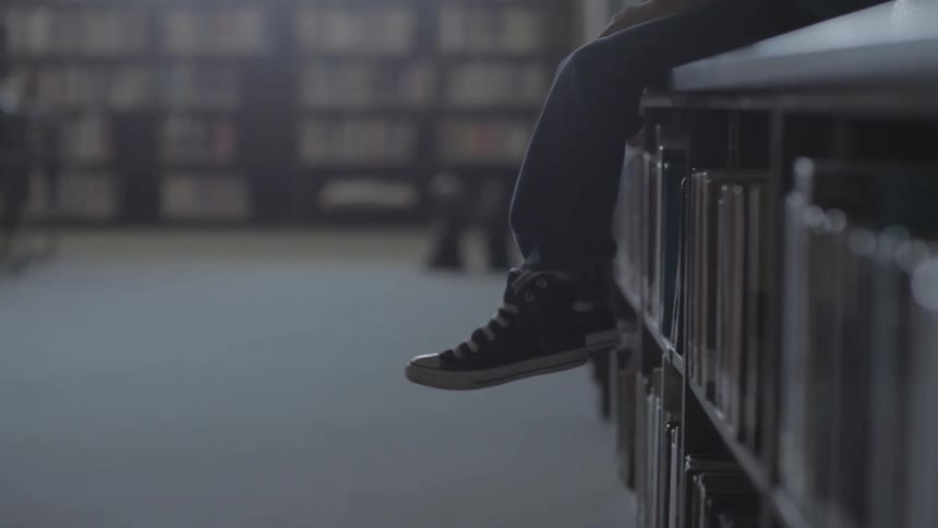 Person sitting on a bookshelf with his feet dangling below