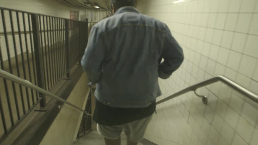 A camera is following a man down the stairs to the subway station