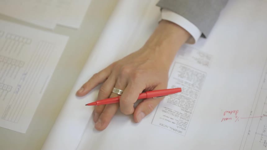 Persons studying an architectural drawing while holding an orange pen in their right hand