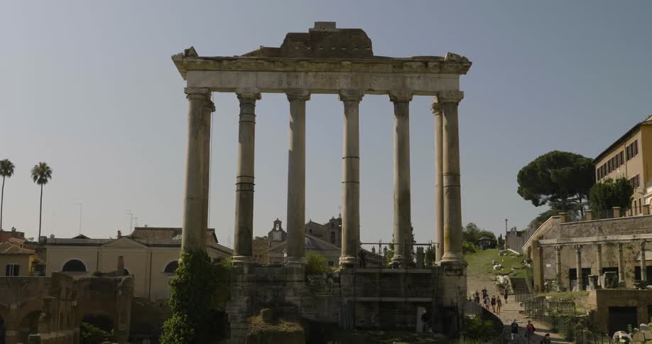 People walking on a sidewalk past ancient ruins