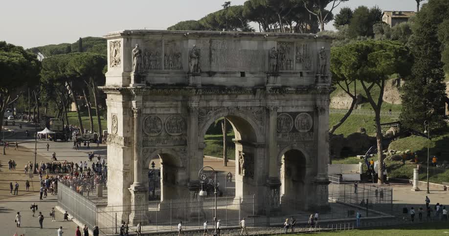 Large stone archway with a fence and tourists around it