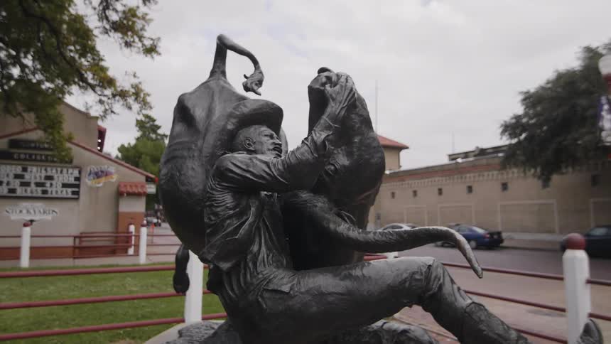 A statue of a man wrestling a bull sits on a lawn