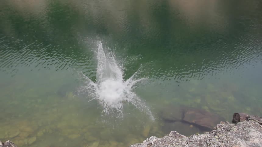 A man jumps off a rock ledge into the water below