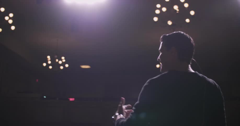 Man talking on stage waves arms enthusiastically