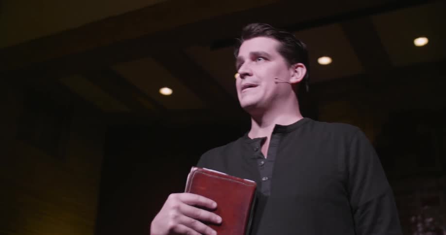 A speaker gives a presentation with a book in hand