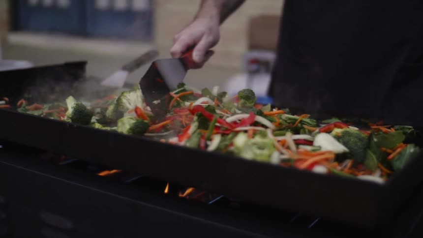 A man spreads vegetables out to cook on a grill