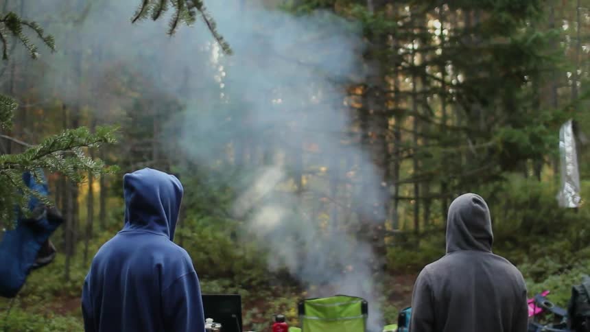 Campers watch smoke rise from a campfire in the woods