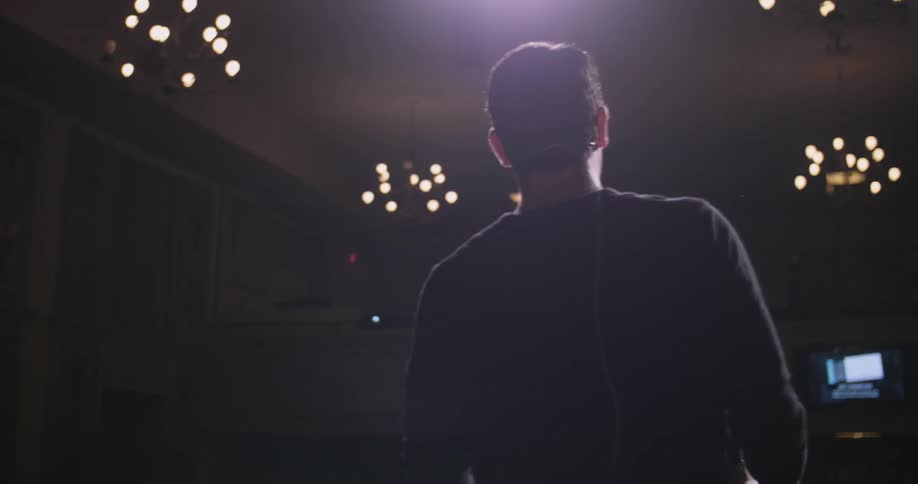 Man gesturing wildly on a stage in a spotlight