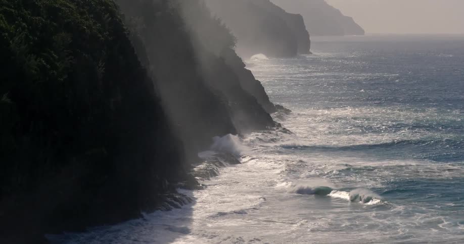 Waves crash against the side of the mountains