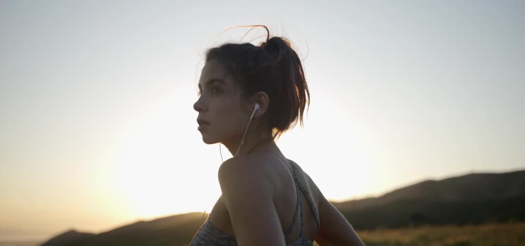 A woman with earbuds in looks around at sunset