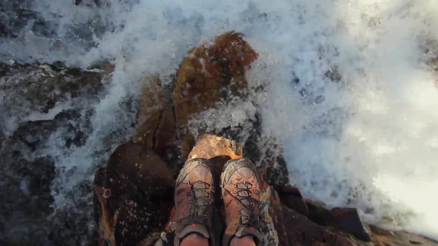 A hiker stands on a rock overlooking a gushing river