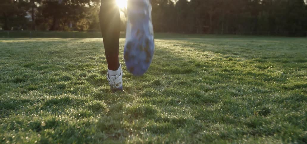 Sneakers kick up water as a person runs in a field