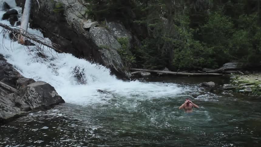 A man jumps and surfaces from a pool of water in a forest