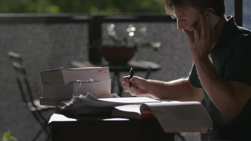 Man on phone writes something in a book
