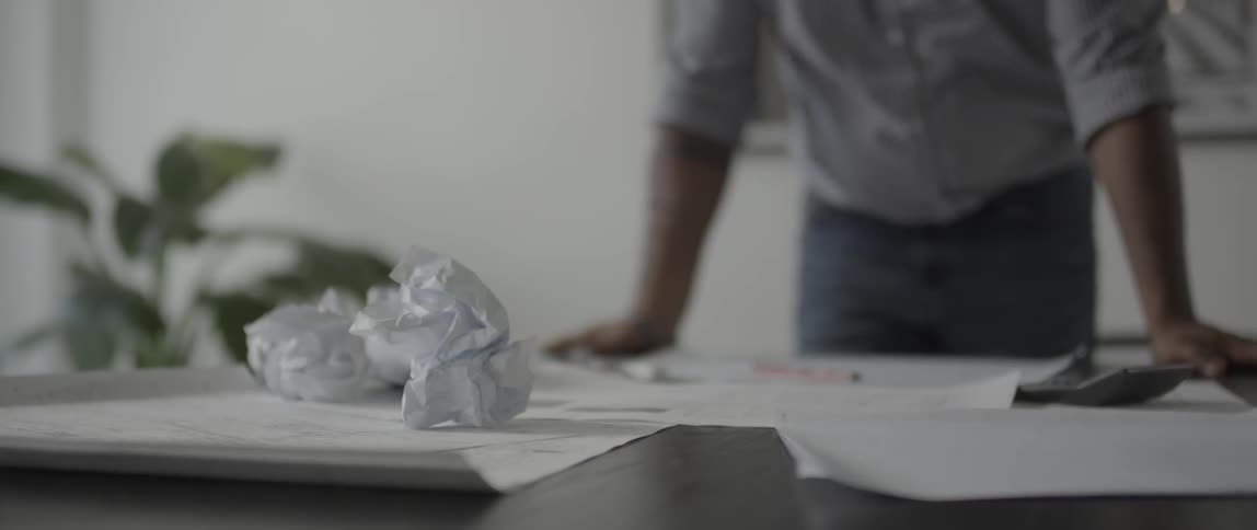 Man leaning on a desk with crumpled balls of paper on it