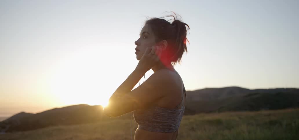 Woman puts earbuds in ears outside on a sunny day