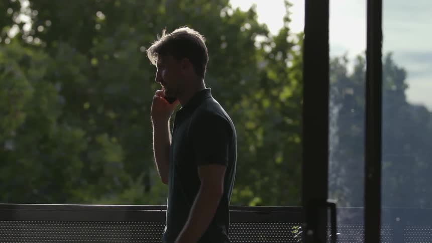 A man stands on a balcony and talks on the phone
