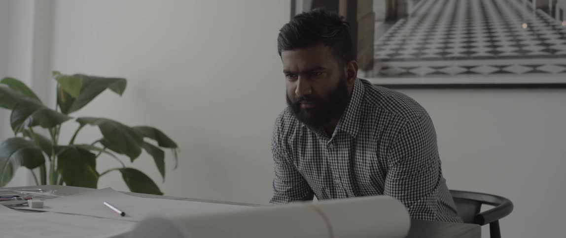 A bearded man looks at a pen on a  table