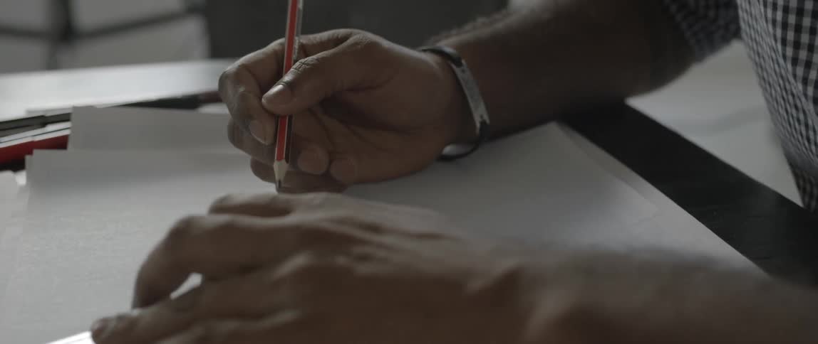 A man uses a pencil and ruler to draw a line on paper