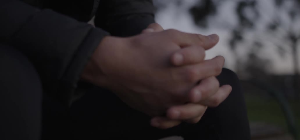 Person sitting on a bench clasping their hands