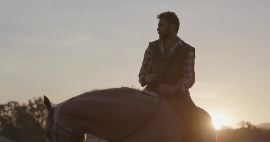 A man sits on a horse as it drinks from a water trough at sunset