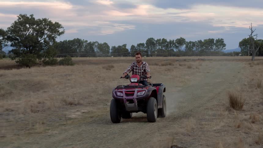 A man is riding a four wheeler down the dirt path