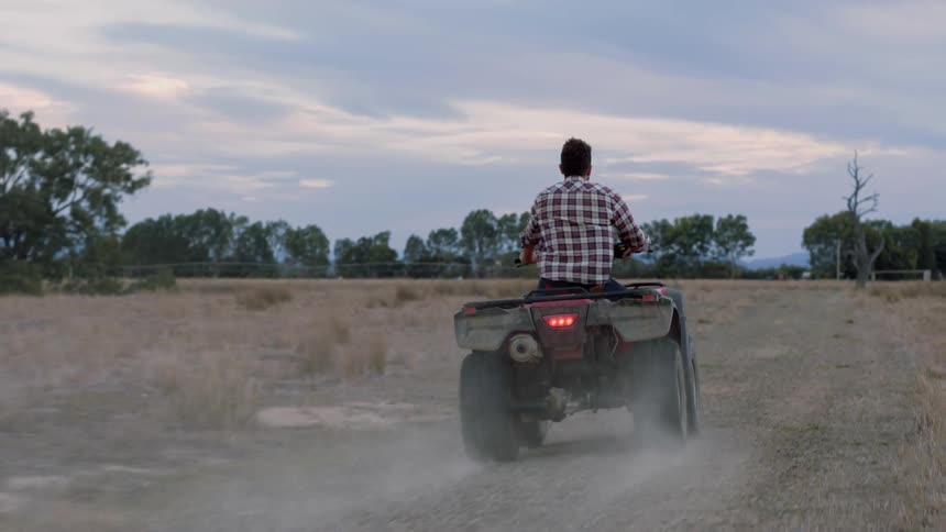 A man rides a quad atv on a dirt path during the day